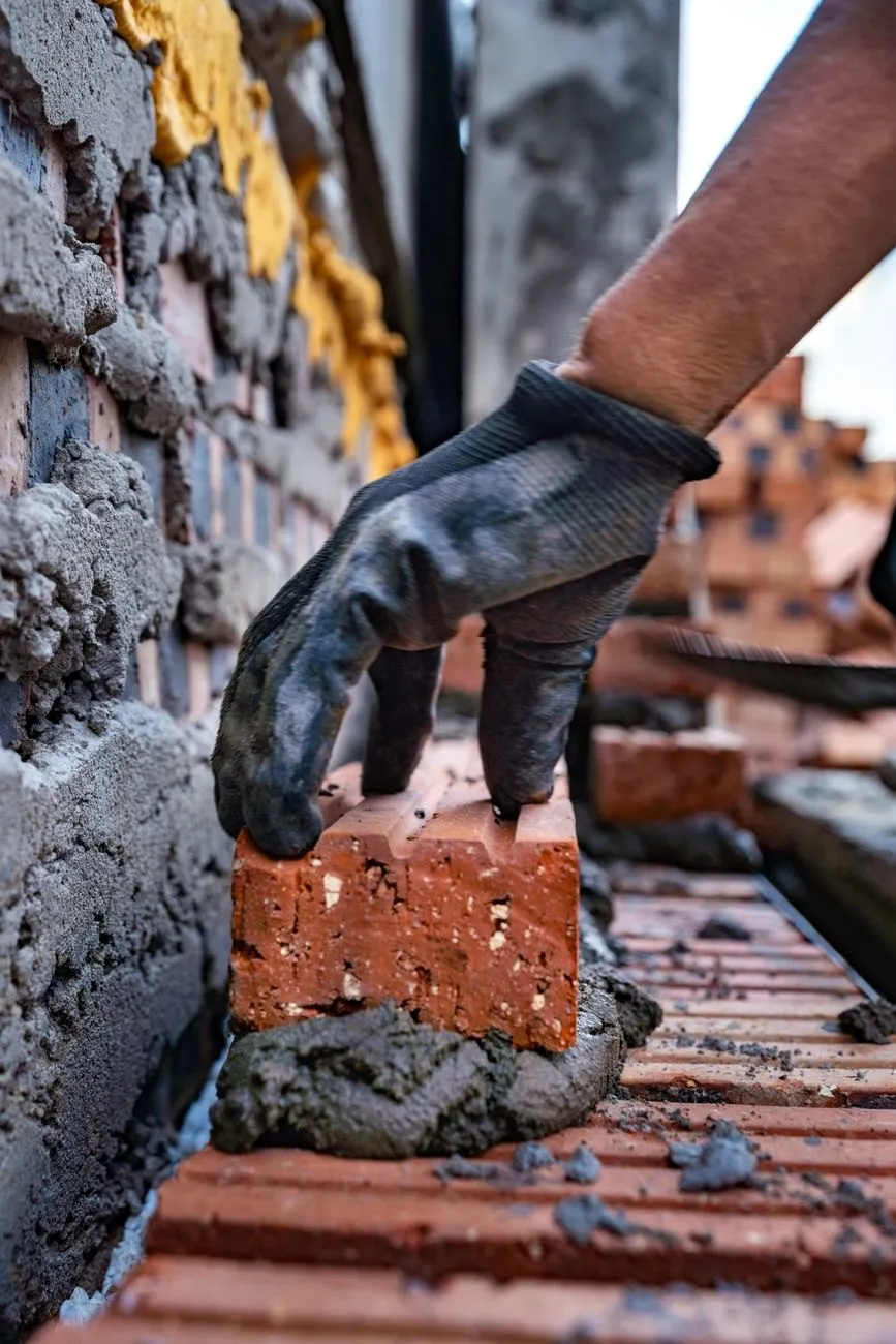 A gloved hand setting a brick into a fresh bed of mortar