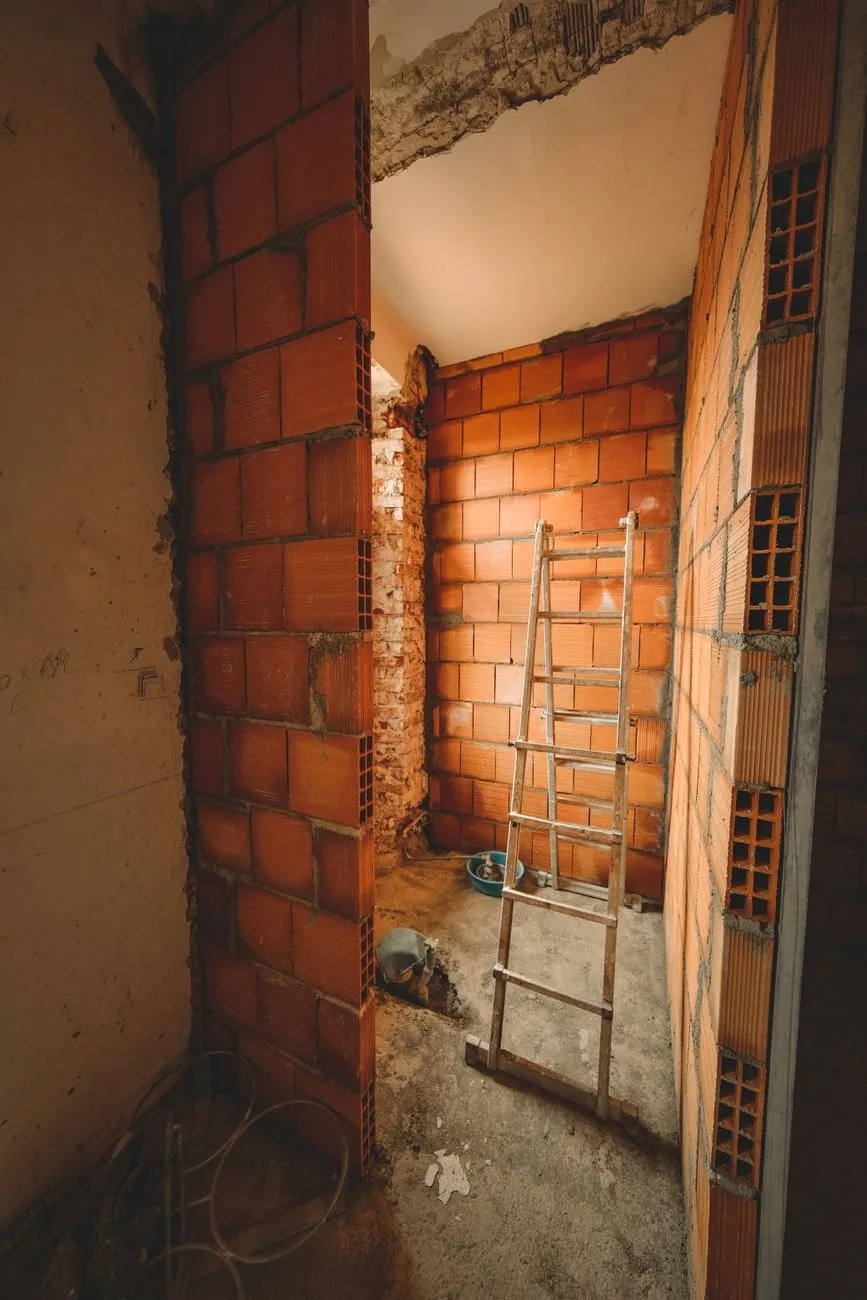 A tall opening formed through a brick wall, a ladder and tools in the room beyond
